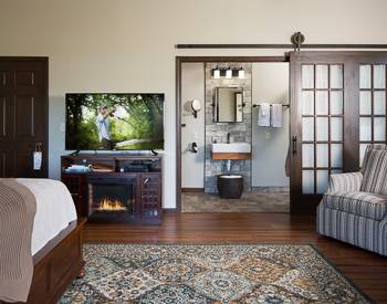 Large tv sitting on a wood cabinet with a built in fireplace, also overlooking the stone bathroom 